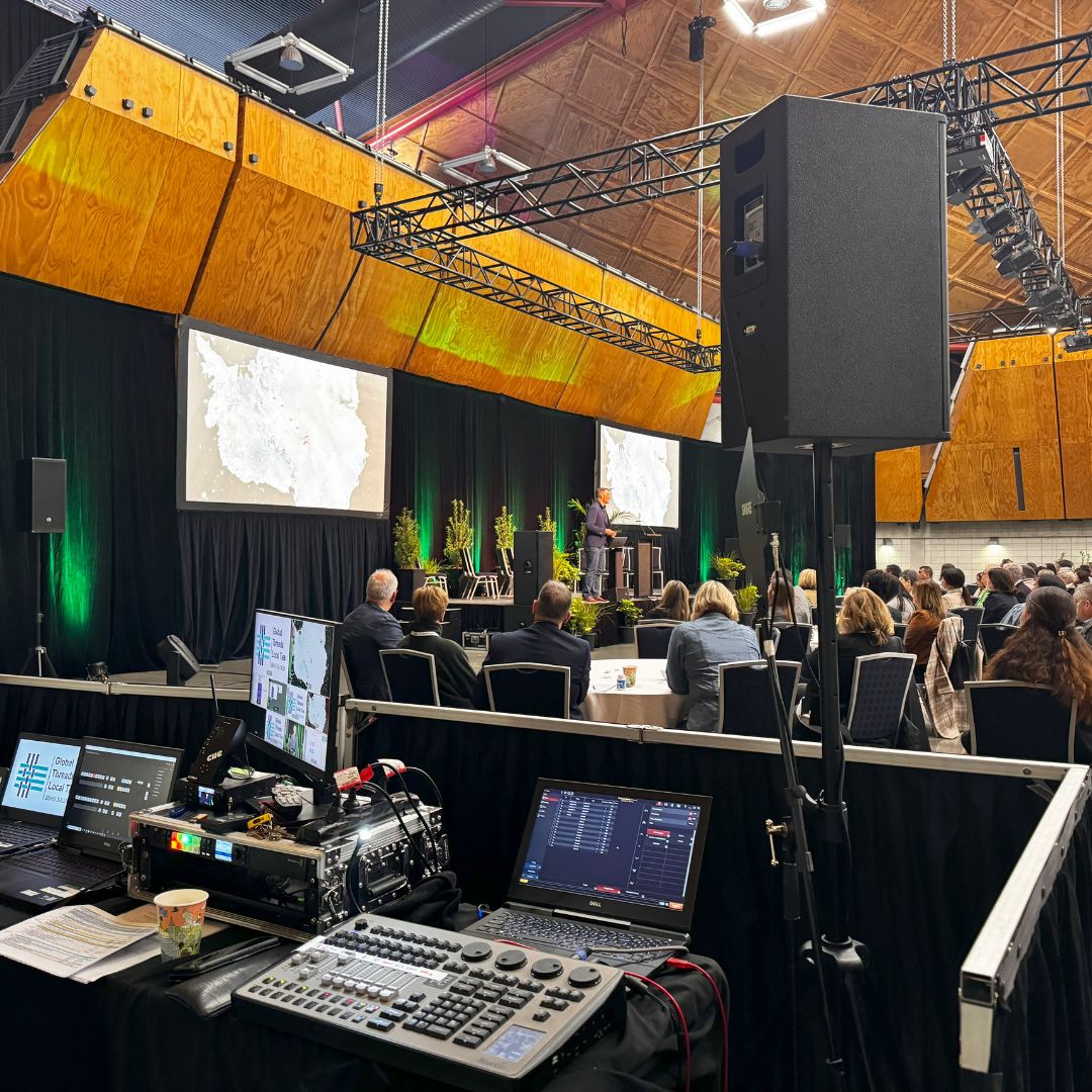 Corporate conference production with professional sound, dual projection screens, stage lighting, and a staffed control position